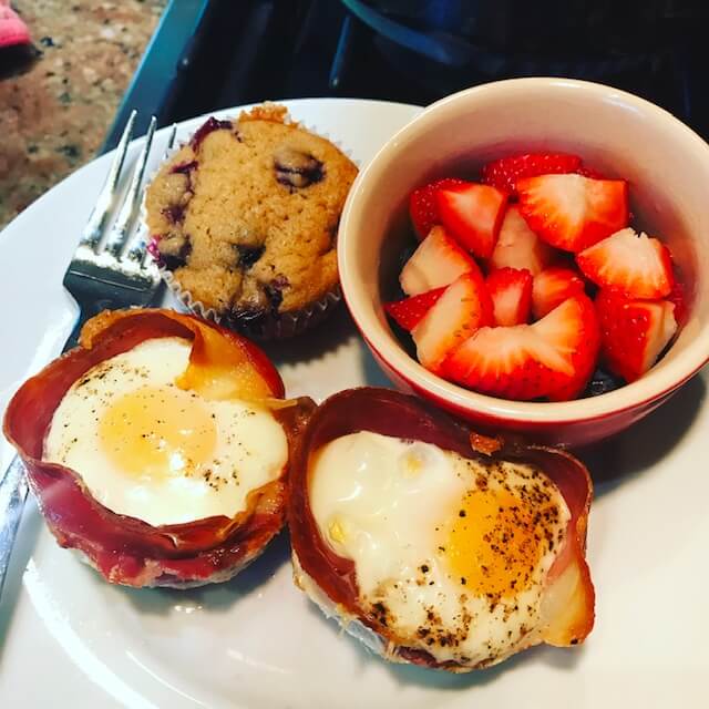Breakfast eggs in prosciutto with blueberry muffin and sliced strawberries